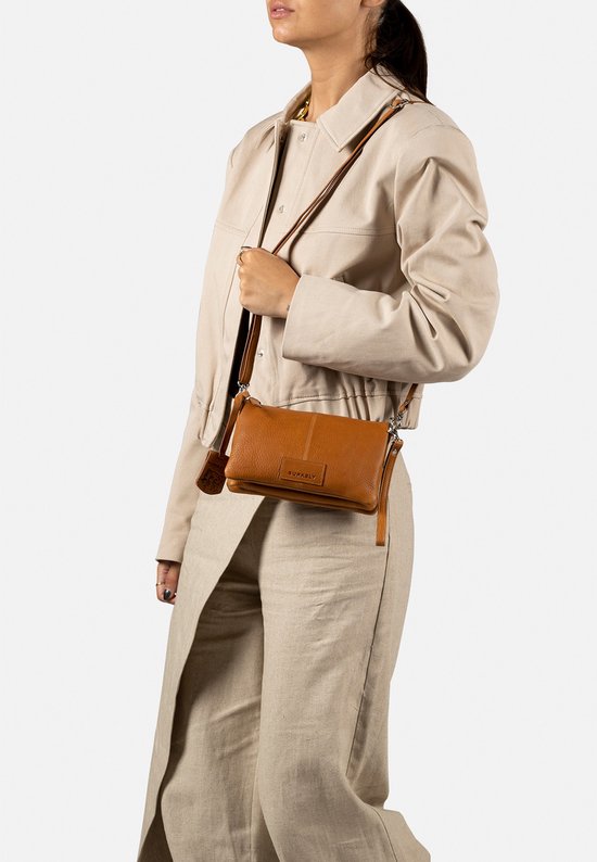 Bruine leren schoudertas gedragen door een model met beige kleding.
