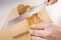 Een hand snijdt een brood met een Wüsthof broodmes op een houten snijplank.