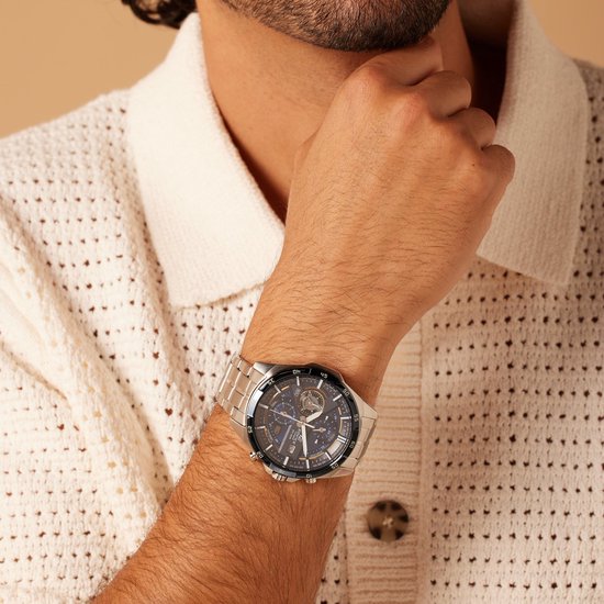 Man draagt een zilverkleurig Edifice horloge met donkerblauwe wijzerplaat, witte kleding.