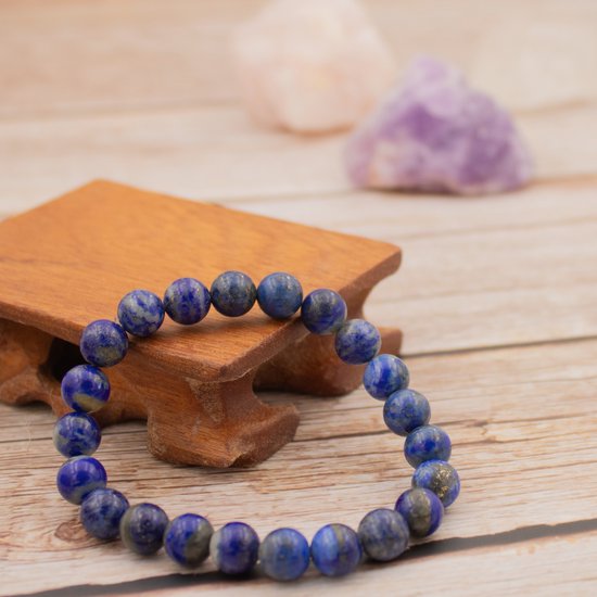 Lapis lazuli armband op een houten display, met roze en paarse kristallen op de achtergrond.