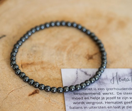 Donkergrijze hematite kralen armband op een houten ondergrond met informatiekaart.