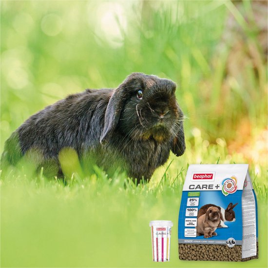 Zwart konijn in gras met zak Beaphar Care+ konijnenvoer en een bakje.