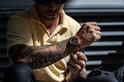 Man met geel poloshirt en tatoeages, die zijn rosegouden Rotorcraft horloge om zijn pols doet.