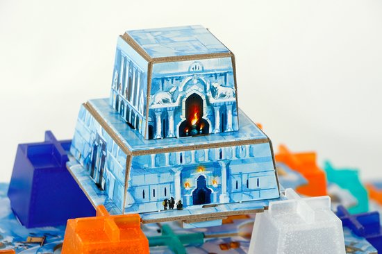 Gedetailleerde close-up van een blauw-wit kartonnen gebouw met leeuwenbeelden en vuur in de ramen, op een blauwe ondergrond met pionnen.