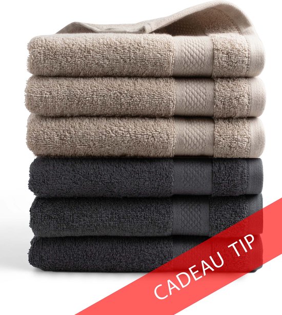 Stapel van zes handdoeken, drie beige taupe en drie antraciet. Zachte textuur met een subtiel patroon aan de rand. Rode band met 'CADEAU TIP'.