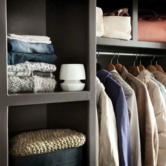 Witte luchtontvochtiger met blauw vochtreservoir, naast opgevouwen kleding op een plank.