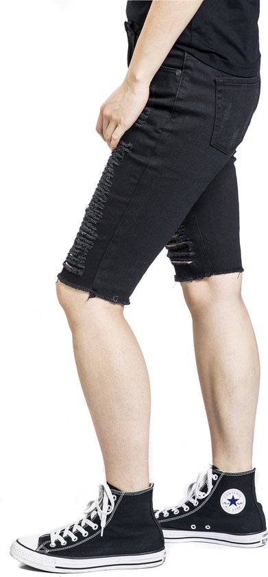 Zijzicht van een vrouw in zwarte, opengescheurde bermudashorts met rafelige zoom.