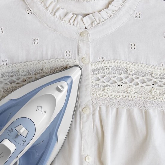 Wit katoenen blouse met broderie anglaise, kant en knopen, met een strijkijzer erop.