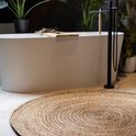 Een rond, natuurlijk jute vloerkleed in een luxe badkamer met een vrijstaand bad.