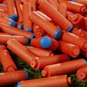 Een hoop oranje Nerf pijltjes met blauwe doppen, verspreid op groen gras.