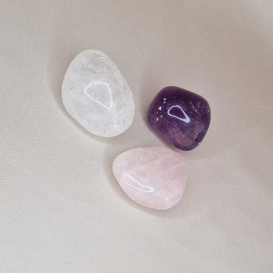 Drie getrommelde edelstenen: rozenkwarts, bergkristal en amethist.