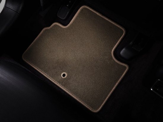 Beige voormat met beige bies geplaatst in de bestuurdersvoetruimte van een auto.