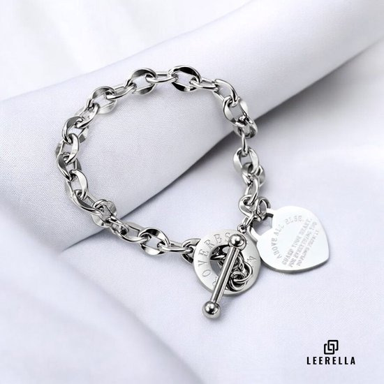 Zilverkleurige schakelarmband met hartvormige hanger met tekst en ronde hanger met tekst. Knevelsluiting, liggend op witte stof.