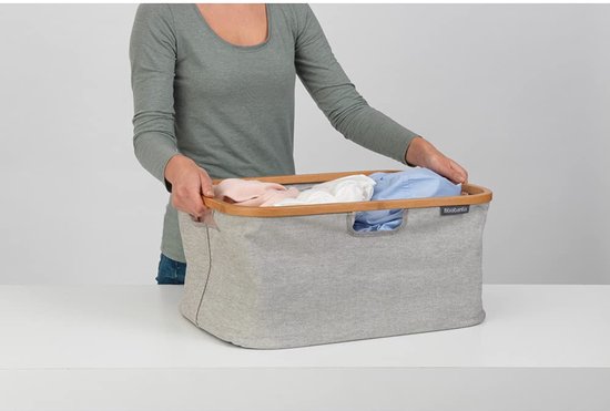Vrouw met grijze Brabantia wasmand gevuld met linnen.
