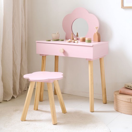 Roze kaptafel met spiegel en stoel, omringd door een witte vloerkleed en een neutrale gordijn.
