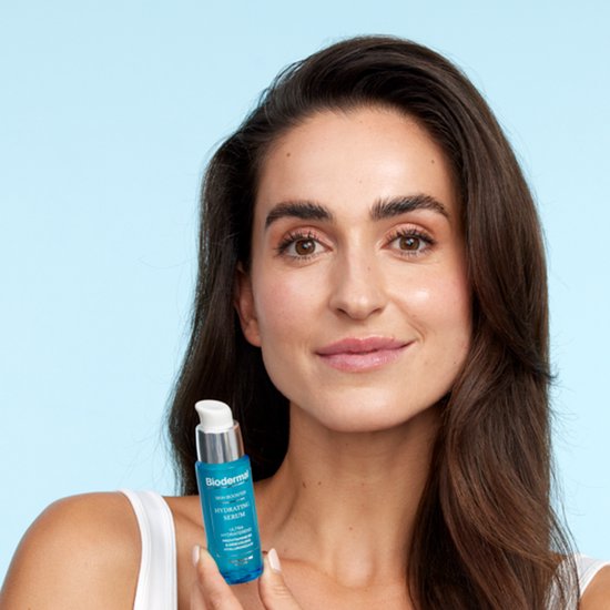 Vrouw met bruin haar houdt een Biodermal Skin Booster Hydrating Serum flesje vast.