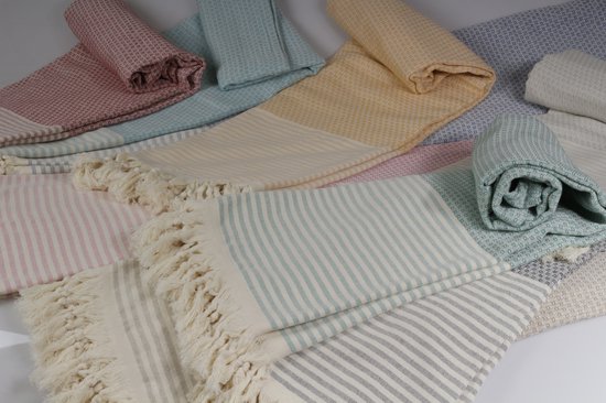 Stapel diverse gekleurde hamamdoeken met strepen en franjes, in kleuren zoals roze, cyaan, geel en grijs.