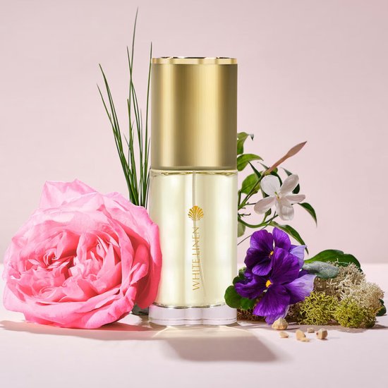 Estée Lauder White Linen Eau de Parfum fles omringd door roze roos, paarse bloemen en mos.