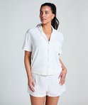 Model in wit pyjamashirt en short, staand met de hand in haar broekzak.