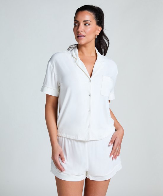 Model in wit pyjamashirt en short, staand met de hand in haar broekzak.