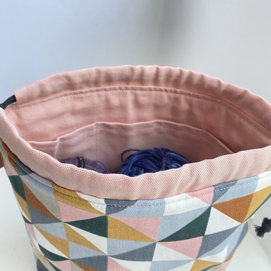 Open projecttas met roze binnenzijde, twee vakjes, wol in blauw en paars, en een geometrisch patroon van roze, oker, terracotta, groen en grijs.