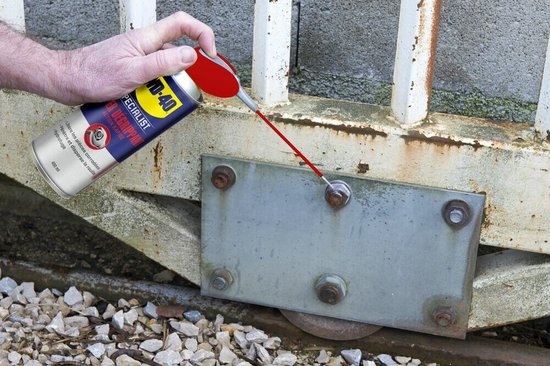 Man spuit WD-40 Specialist Super Kruipolie op de scharnieren van een metalen poort.