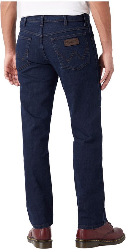 Achterkant van een man in een donkerblauwe Wrangler jeans met een bruin leren logolabel.