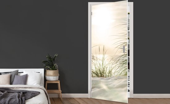 Een deursticker met een zonsondergang boven de duinen, zand en wuivend gras.