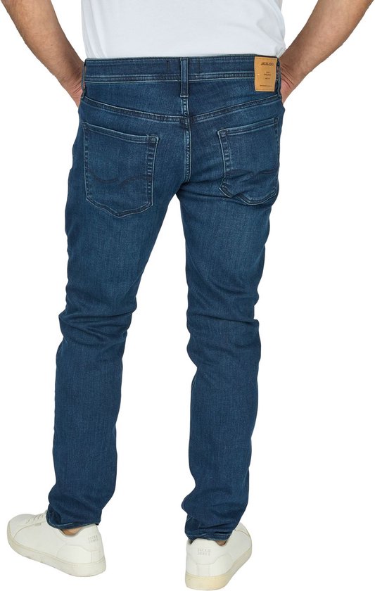 Man in een slanke, donkerblauwe spijkerbroek, achterkant, witte sneakers.