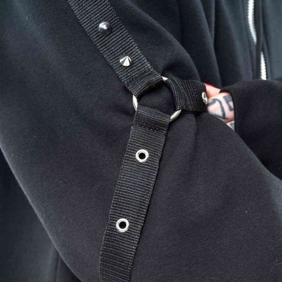 Detail van de mouw van een zwarte hoodie met een stoffen band, studs en een metalen ring.