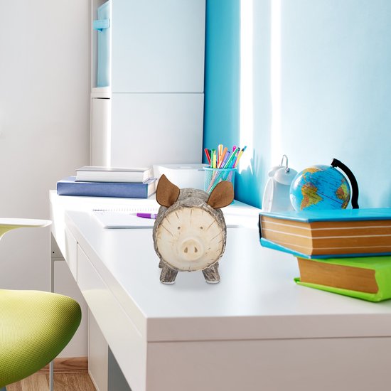 Een spaarvarken met een schorslook, staand op een bureau tussen boeken en een wereldbol.