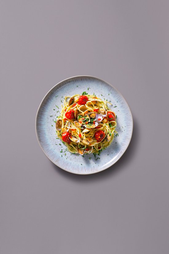 Bovenaanzicht van een Palmer bord met een pasta gerecht van venusschelpen, kerstomaatjes en kruiden.