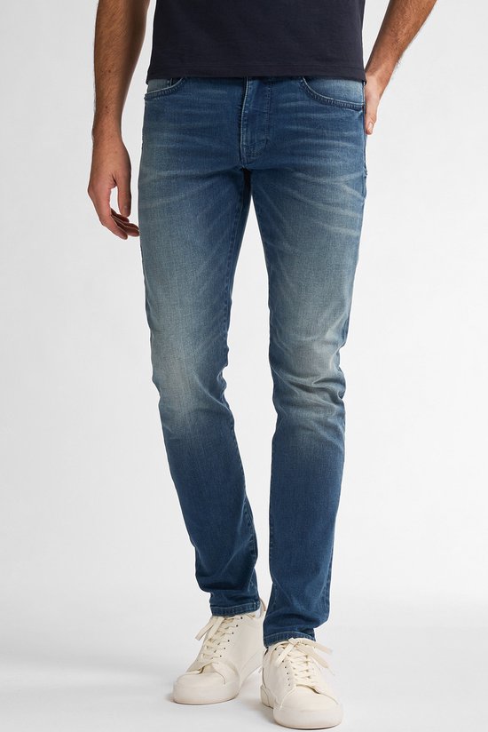 Man die staat in een vaalblauwe slim fit spijkerbroek met een marineblauw t-shirt.