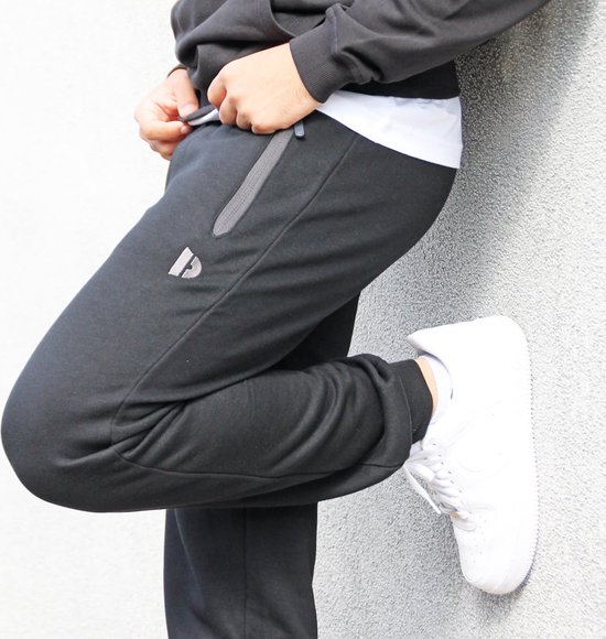 Model in een zwarte joggingbroek, met witte sneakers.