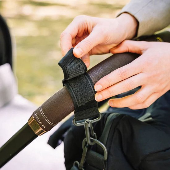 Mains attachant un clip noir pour poussette au guidon d'une poussette.