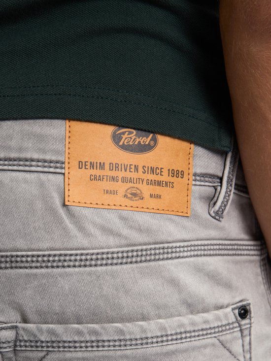 Close-up van het bruine leren Petrol Industries label op de achterkant van een grijze denim short. De tekst 'DENIM DRIVEN SINCE 1989' is zichtbaar.