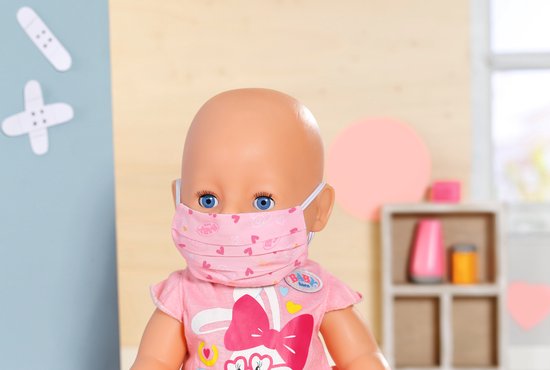Close-up van een baby Born pop met een roze masker met hartjespatroon en een dokterstas-badge.