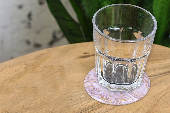 Sous-verre rond à motif marbre lilas et or, sous un verre d'eau sur une table en bois.