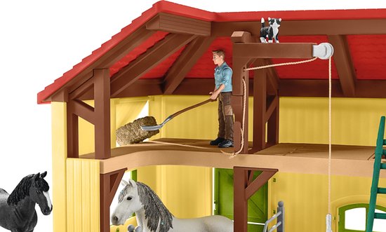 Speelgoed paardenstal met een man op een ladder, twee paarden en hooi.