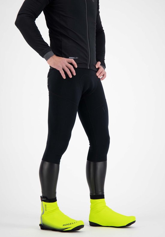 Een man staat met de handen in de zij, draagt zwarte fietskleding en fluor gele overschoenen.