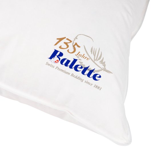 Close-up van het Balette logo op een wit donzen kussen, met opschrift '135 Jahre Balette Swiss Premium Bedding since 1881'.