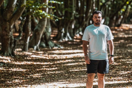 Homme portant un t-shirt de sport blanc Rogelli et un short noir, debout sur un chemin forestier.