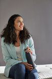 Vrouw met krullend haar, gekleed in een lichtblauwe blazer, houdt een zwarte thermosfles vast.