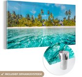 MuchoWow® Glasschilderij 80x40 cm - Schilderij acrylglas - Uitzicht op een strand met palmbomen vanuit het water - Foto op glas - Schilderijen