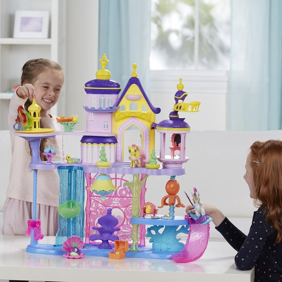 Twee meisjes spelen vrolijk met een paars, roze en geel My Little Pony kasteel.