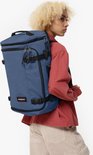 Vrouw met blond krullend haar draagt een donkerblauwe Eastpak reistas op haar rug.