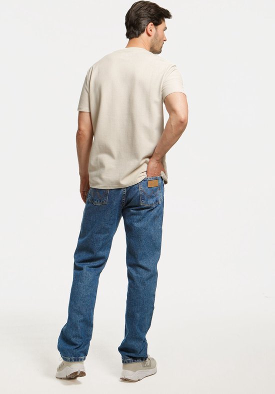 Man in een beige shirt en rechte blauwe jeans, van achteren gezien.