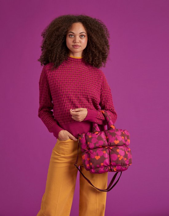Model met een puffy handtas met paarse en oranje bloemenprint, gedragen met een roze trui en gele broek.