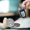 Zilveren CR2430 3V lithium knoopcel batterij naast een zwarte autosleutel.