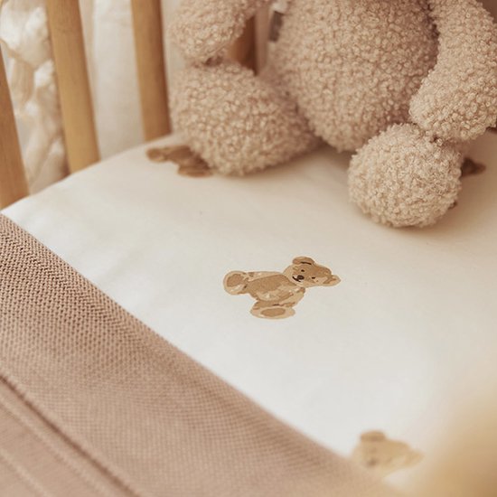 Drap de lit crème à imprimé ours en peluche, avec une couverture tricotée beige au premier plan.